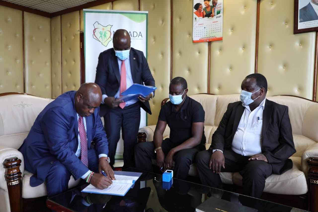 Signing the MoU, Mr. Victor Okioma, CEO NACADA (left), Mr. Daniel K’Onyango, NACADA Corporation Secretary (standing) and Mr. Richard Terer, Director, Bomet County Liquor Board (far right)