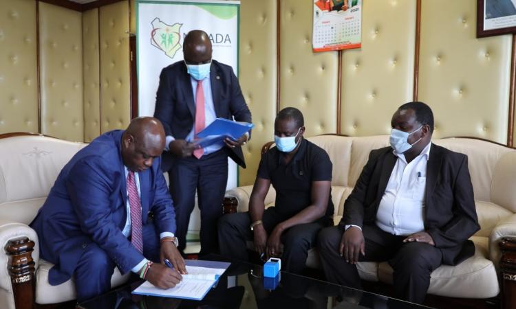 Signing the MoU, Mr. Victor Okioma, CEO NACADA (left), Mr. Daniel K’Onyango, NACADA Corporation Secretary (standing) and Mr. Richard Terer, Director, Bomet County Liquor Board (far right)